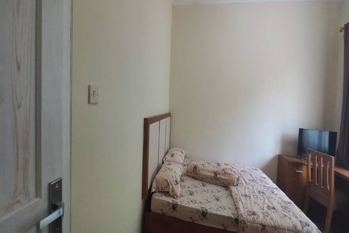 A bedroom with a bed, a wooden nightstand, a television, and a wooden chair.
