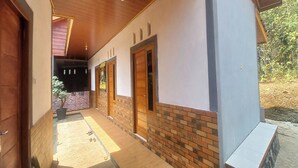 A covered corridor with wooden doors and a brick wall. - Hotel O Homestay Gua Pindul Kang Haris (Karangmojo)