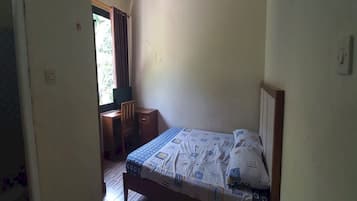 A bedroom with a bed, a desk, and a window with curtains.