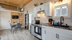 Una cocina moderna con armarios blancos, electrodomésticos de acero inoxidable, un comedor con mesa y sillas, y techo de madera.