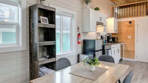 Una cocina moderna con armarios blancos, techo de madera y comedor con mesa y sillas de madera.