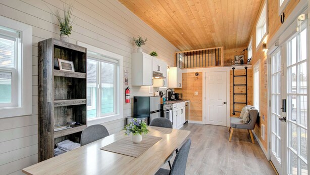 Habitación con paneles de madera, una mesa de comedor, sillas, una pequeña cocina y un altillo accesible por una escalera.