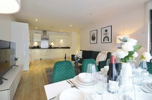 Un salon moderne avec un coin repas, une cuisine à l’arrière-plan et un téléviseur sur le côté gauche.
