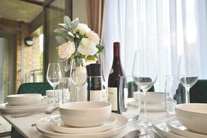 A table set for dining with white plates, bowls, and wine glasses, a bottle of wine, and a vase with flowers. - Modern 2 Bedroom Apartment Steps from Vauxhall St (Greater London)