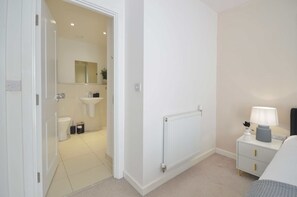 Une salle de bain moderne avec des toilettes, un lavabo et un miroir. Il y a un radiateur au mur et une table de chevet avec une lampe.