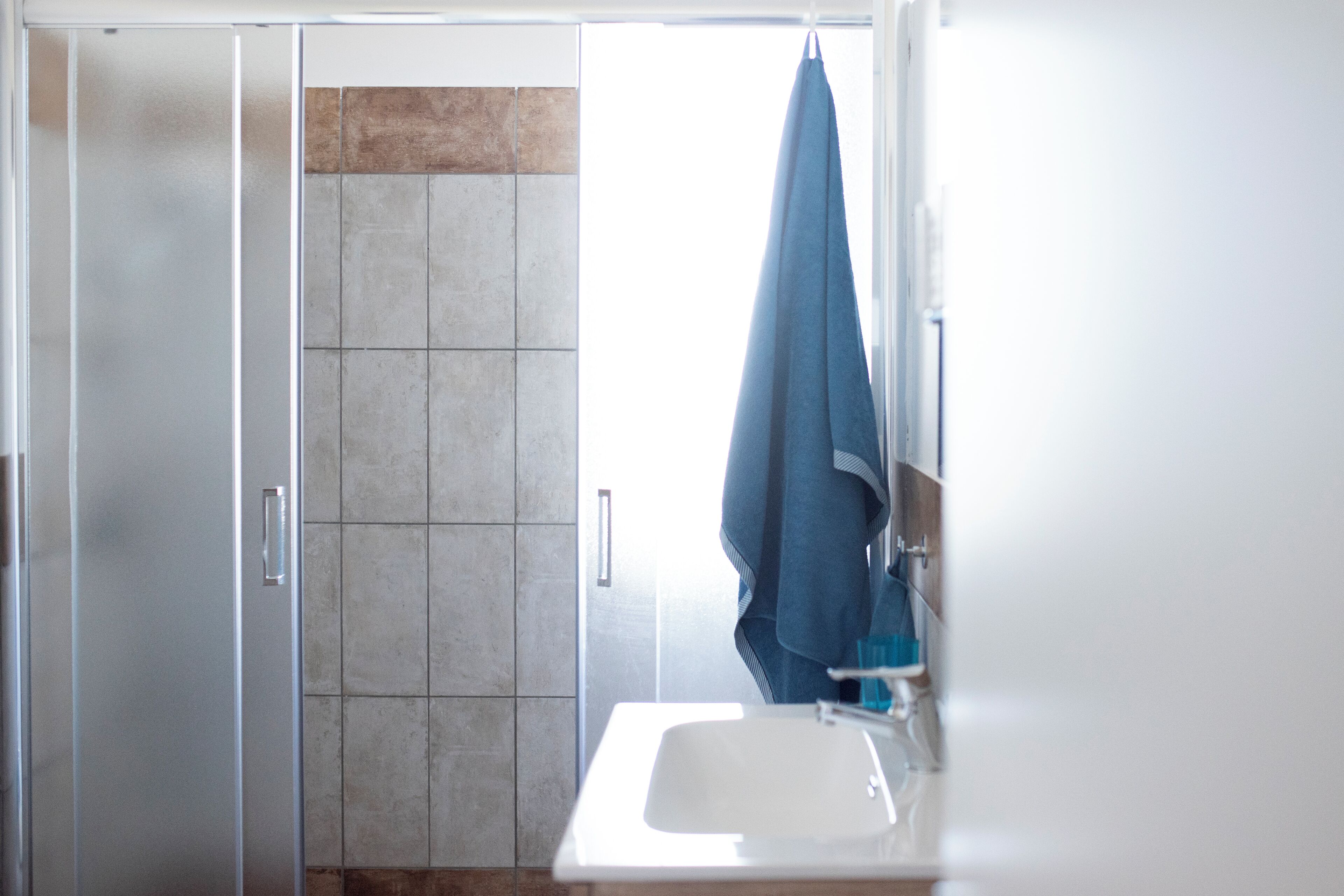 A bathroom with a glass shower door, a white sink, and a towel hanging on the wall.
