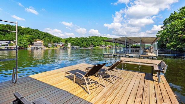 A wooden dock with lounge chairs and a covered area, overlooking a lake with houses in the background. - The Lake Shack Waterfront Life (Camdenton)