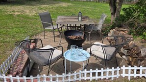 Une terrasse extérieure avec une table et des chaises, un foyer et une clôture blanche en bois.