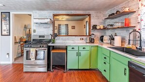 Une cuisine moderne dotée d’une cuisinière en acier inoxydable, de meubles de rangement verts, d’un four encastré et d’un lave-vaisselle.