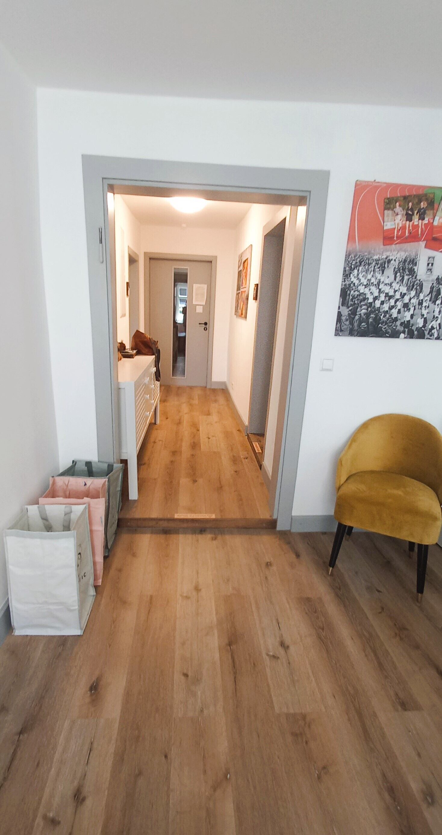 Un corridoio con pavimento in legno, una sedia gialla e una porta che dà su un'altra stanza.