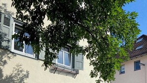 An outdoor seating area with tables and chairs, a large umbrella, and a building with windows and shutters. - Hostel  Altes Spital Balingen (Balingen)