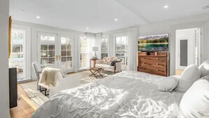 Een ruime slaapkamer met een groot bed, een houten dressoir en een zithoek met een stoel en een klein tafeltje.