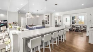 Een moderne keuken met een centraal eiland, barstoelen, hanglampen en een eethoek met een tafel en stoelen.