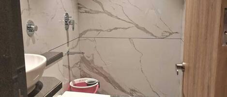 A bathroom with a marble wall, a toilet, a sink, and a shower area.