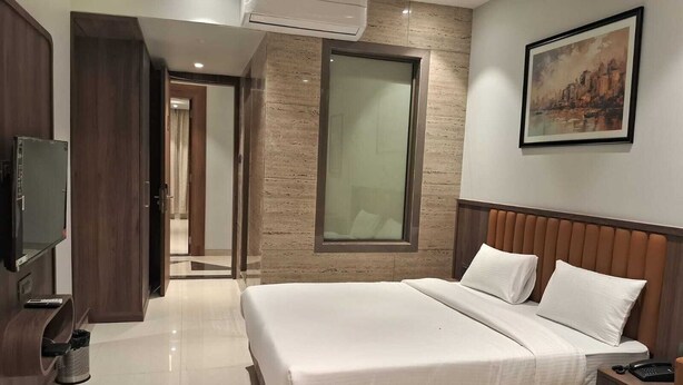 Una habitación de hotel moderna con una cama grande, televisión, un cuadro en la pared y vista a la ciudad.