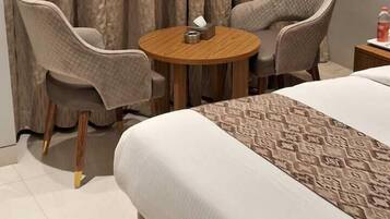 A hotel room with a large bed, two armchairs, a small round table, and a curtain backdrop.