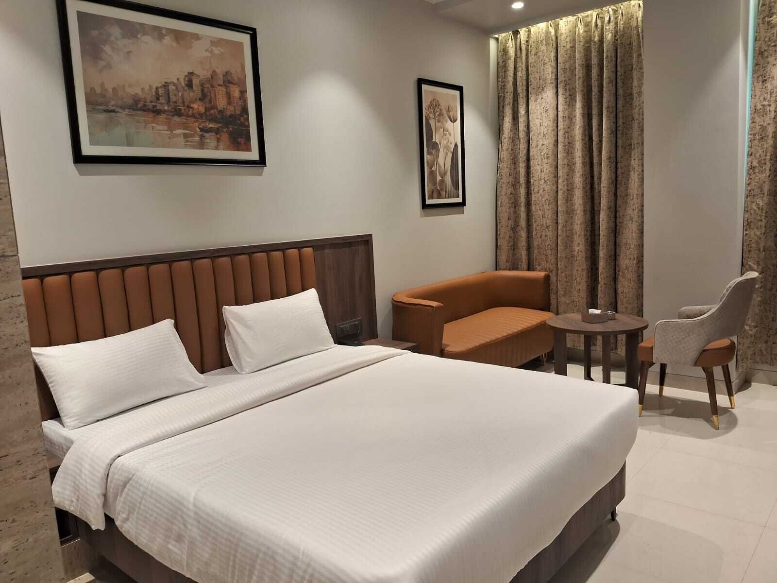 A hotel room with a large bed, a chair, a small table, and two framed pictures on the wall.