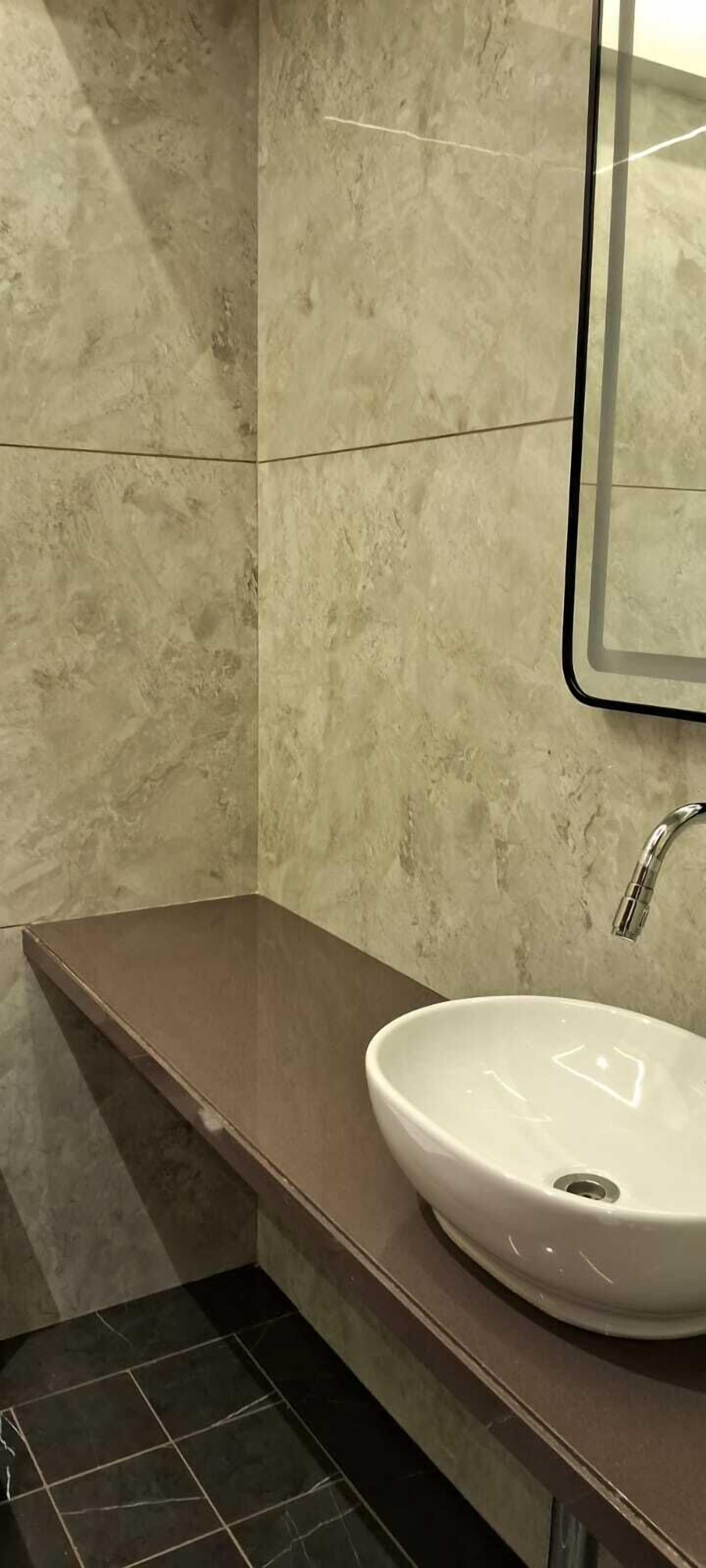 A bathroom with a marble wall, a brown countertop, and a white sink with a single faucet.