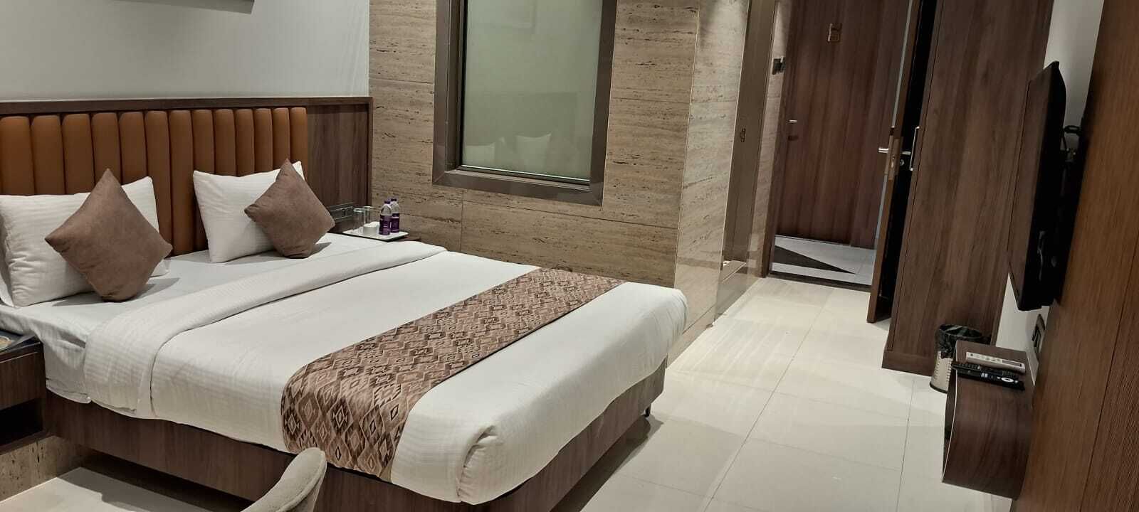Een moderne hotelkamer met een groot bed, een houten hoofdbord, een nachtkastje met een fles en glazen, en een groot raam.