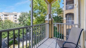 Een balkon met een stoel, uitzicht op een parkeerplaats en een gebouw met balkons op de achtergrond.