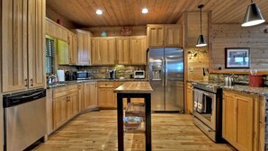 A kitchen with wooden cabinets, a stainless steel refrigerator, a wooden table, and a stone backsplash. - Sunset Pointe | Epic Views + Hot Tub + Games (Mineral Bluff)