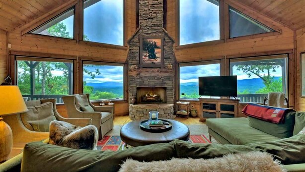 A cozy cabin interior with a stone fireplace, large windows, and comfortable seating. - Sunset Pointe | Epic Views + Hot Tub + Games (Mineral Bluff)