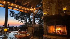An outdoor dining area with a stone fireplace, string lights, and a view of the landscape. - Sunset Pointe | Epic Views + Hot Tub + Games (Mineral Bluff)