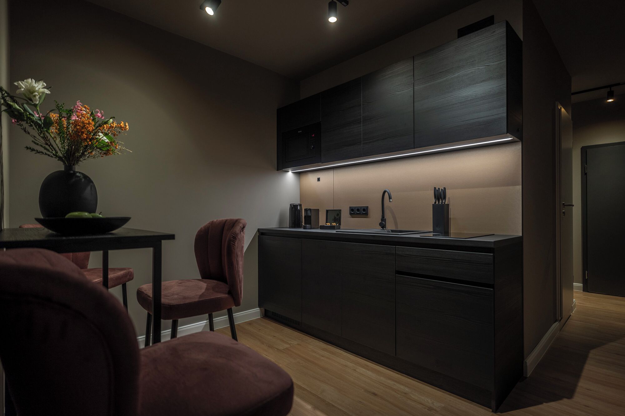 A modern kitchen with dark cabinetry, a central island, and a vase with flowers on a table.