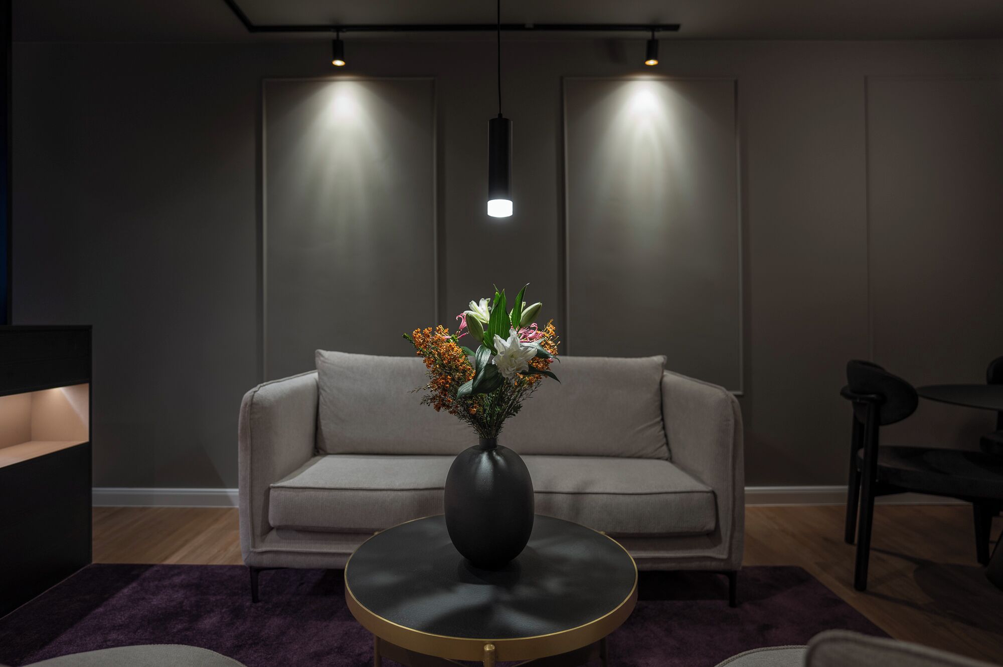 A modern living room with a grey sofa, a round black coffee table, and a vase of flowers.
