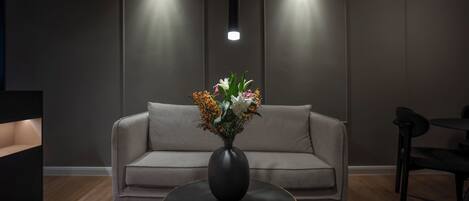 Una sala de estar moderna con un sofá gris, una mesa de centro redonda negra y un jarrón con flores.