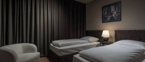 A hotel room with two single beds, a sofa, a nightstand with a lamp, and a painting on the wall.