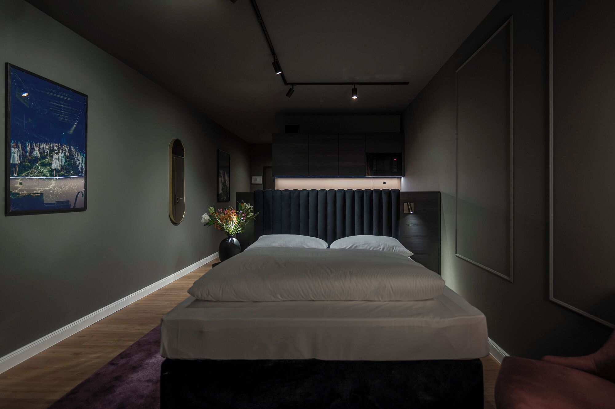 A modern bedroom with a bed, a small side table, a vase with flowers, and a framed picture on the wall.