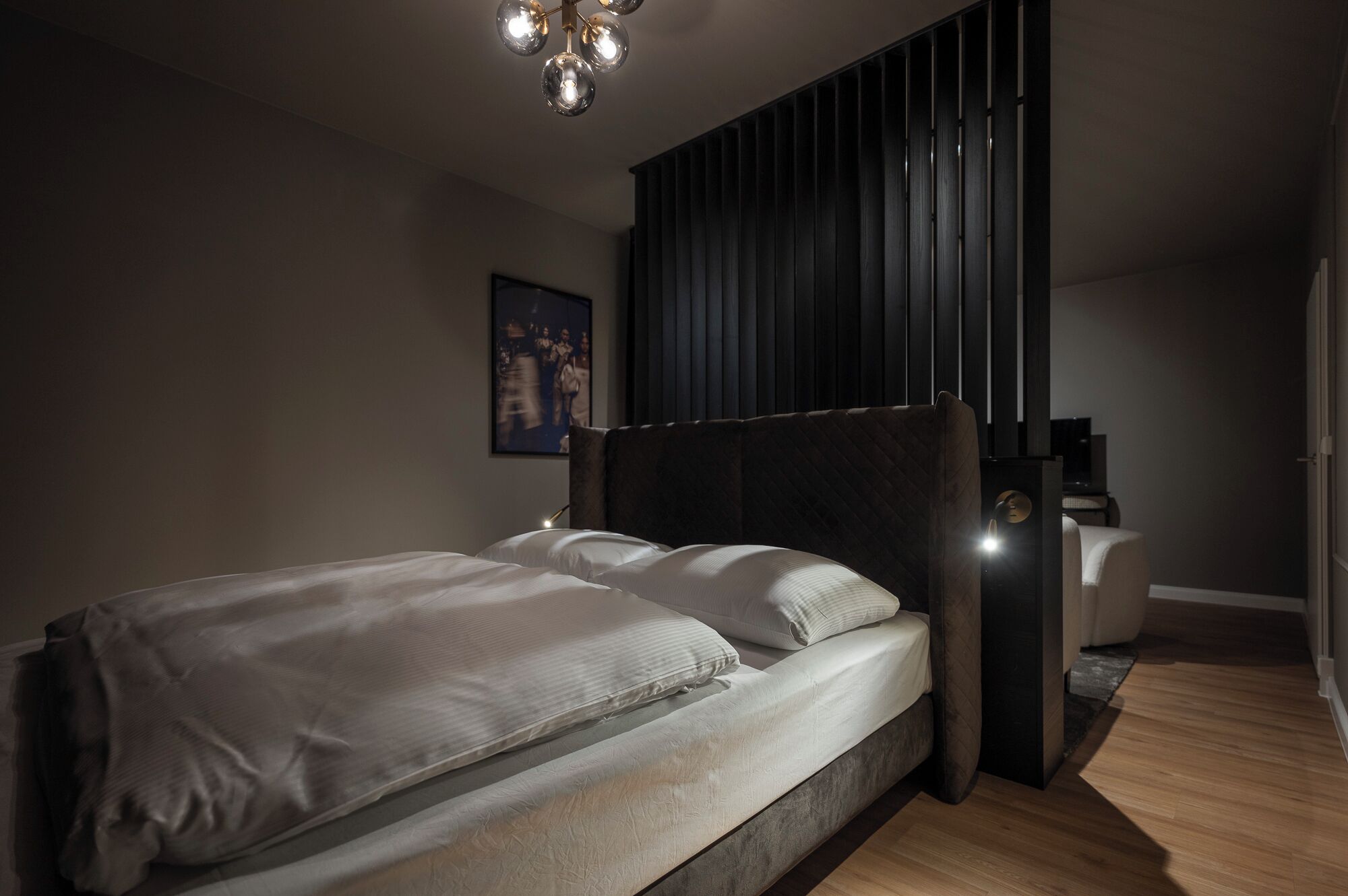 Una camera da letto moderna con un letto grande, una testata scura, un comodino e una lampada a parete.