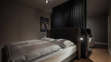 A modern bedroom with a large bed, a dark headboard, a nightstand, and a wall-mounted light fixture.