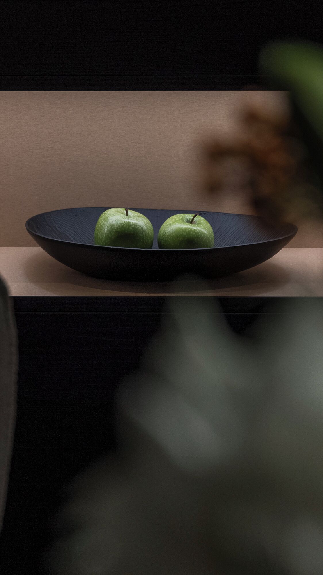 A dark blue plate with two green apples on a wooden surface.