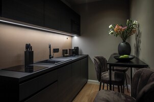 Una cocina moderna con armarios oscuros, encimera negra y microondas integrado. Hay un florero con flores sobre una mesa junto a la cocina.