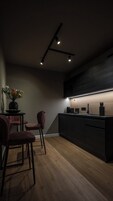 Una cocina moderna con encimera oscura, suelo de madera y lámpara colgante.