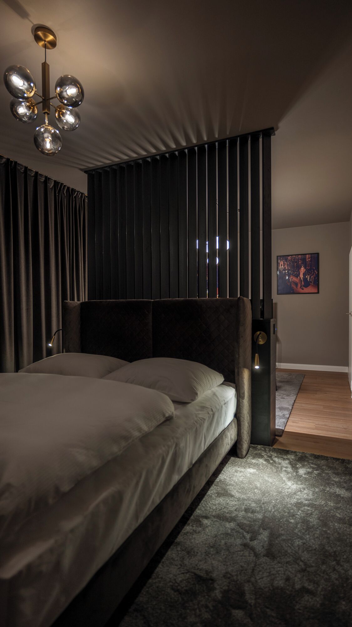 Un dormitorio moderno con una cama grande, cortinas oscuras, una lámpara de techo original y un cuadro enmarcado en la pared.