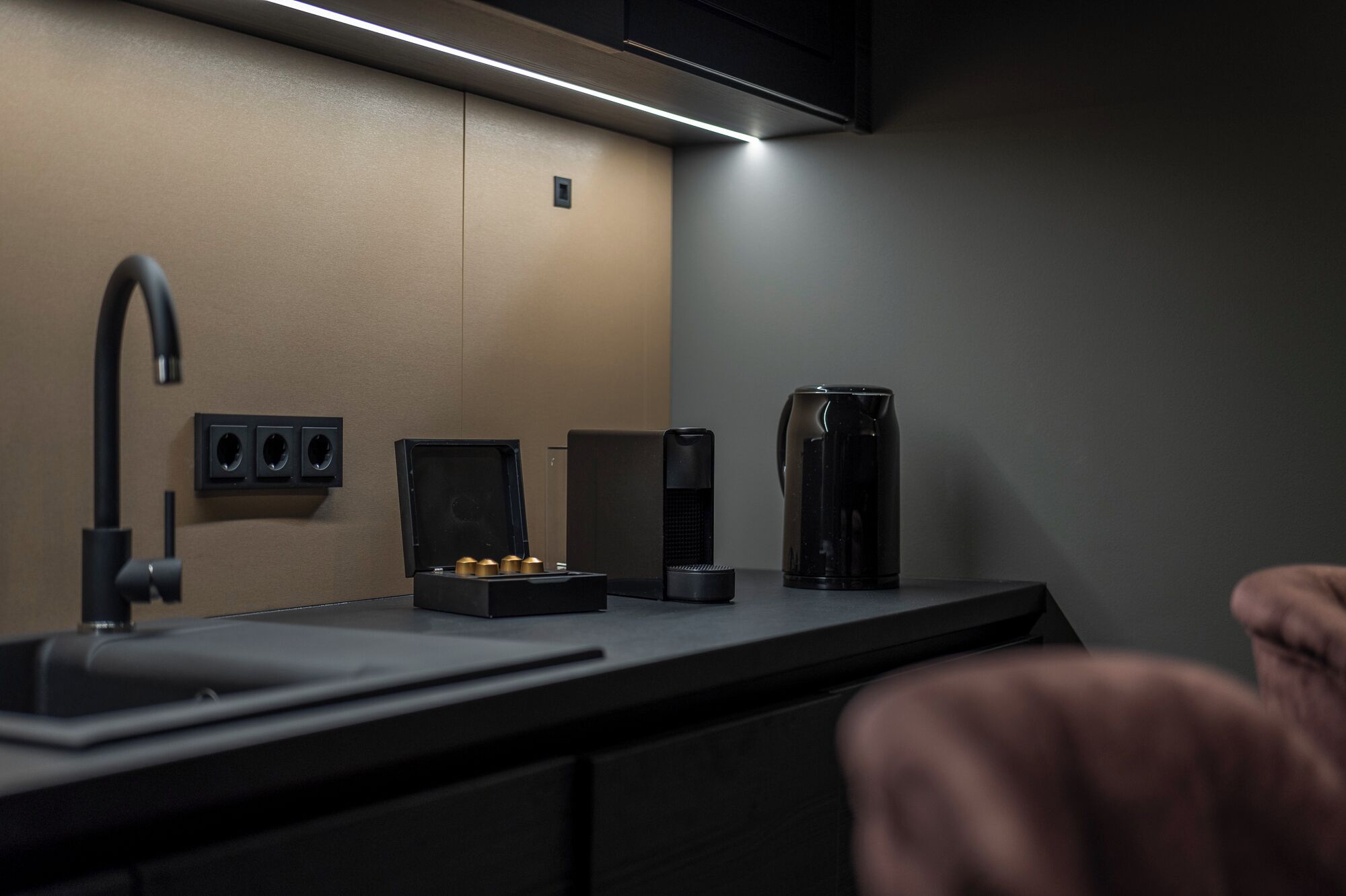 Una cocina moderna con encimera negra, un lavamanos, una cafetera y un altavoz.