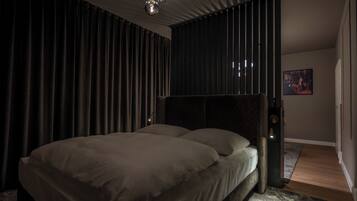 Een moderne slaapkamer met een groot bed, donkere gordijnen en een kroonluchter.