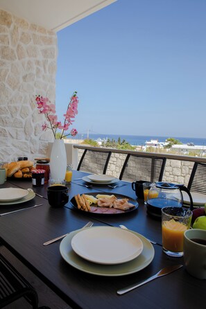 Enjoy a serene breakfast on the balcony with a stunning sea view, surrounded by a beautifully set table and fresh flowers.