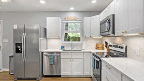 A modern kitchen with white cabinets, stainless steel appliances, and a marble countertop.
