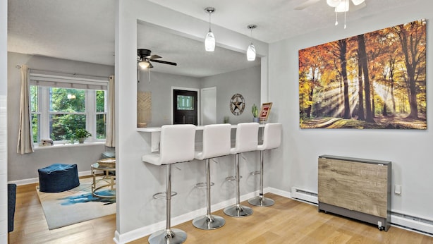 A modern kitchen with a bar area, a ceiling fan, and a large window.