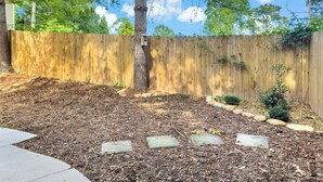 A backyard with a wooden fence, a tree, and a small bush.