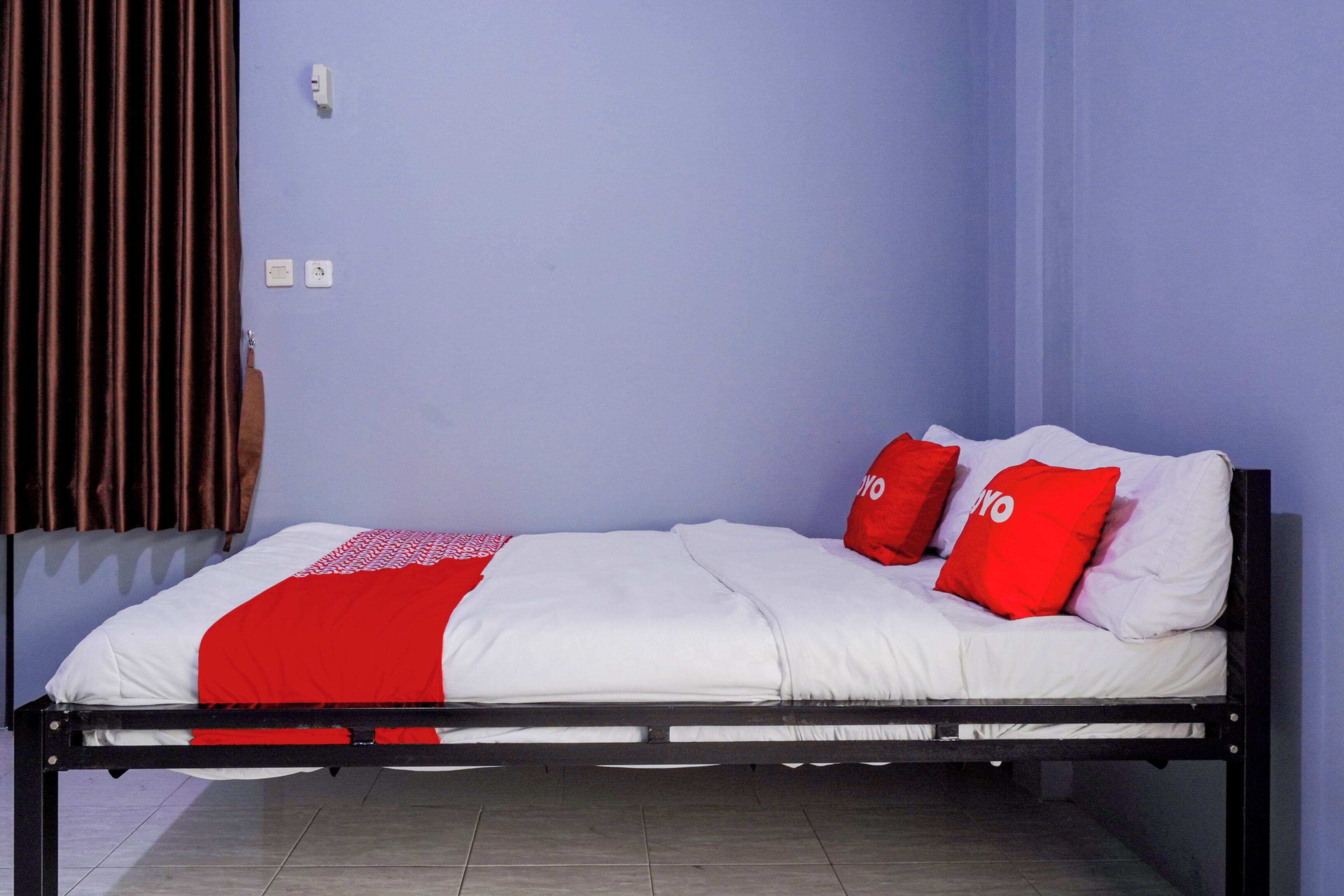 A single bed with a black frame, white bedding, and two red pillows.