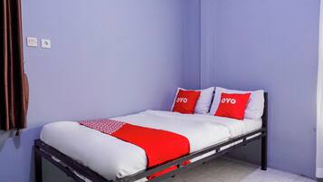 Uma cama de solteiro com colcha vermelha e branca, duas almofadas vermelhas com a palavra "OYO" estampada e uma cortina marrom no lado esquerdo.
