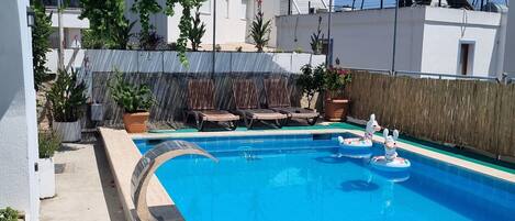 Una piscina con sillas de descanso y un pequeño flotador.
