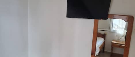 A bedroom with a bed, a small wooden stool, a heater, a TV mounted on the wall, and a mirror.