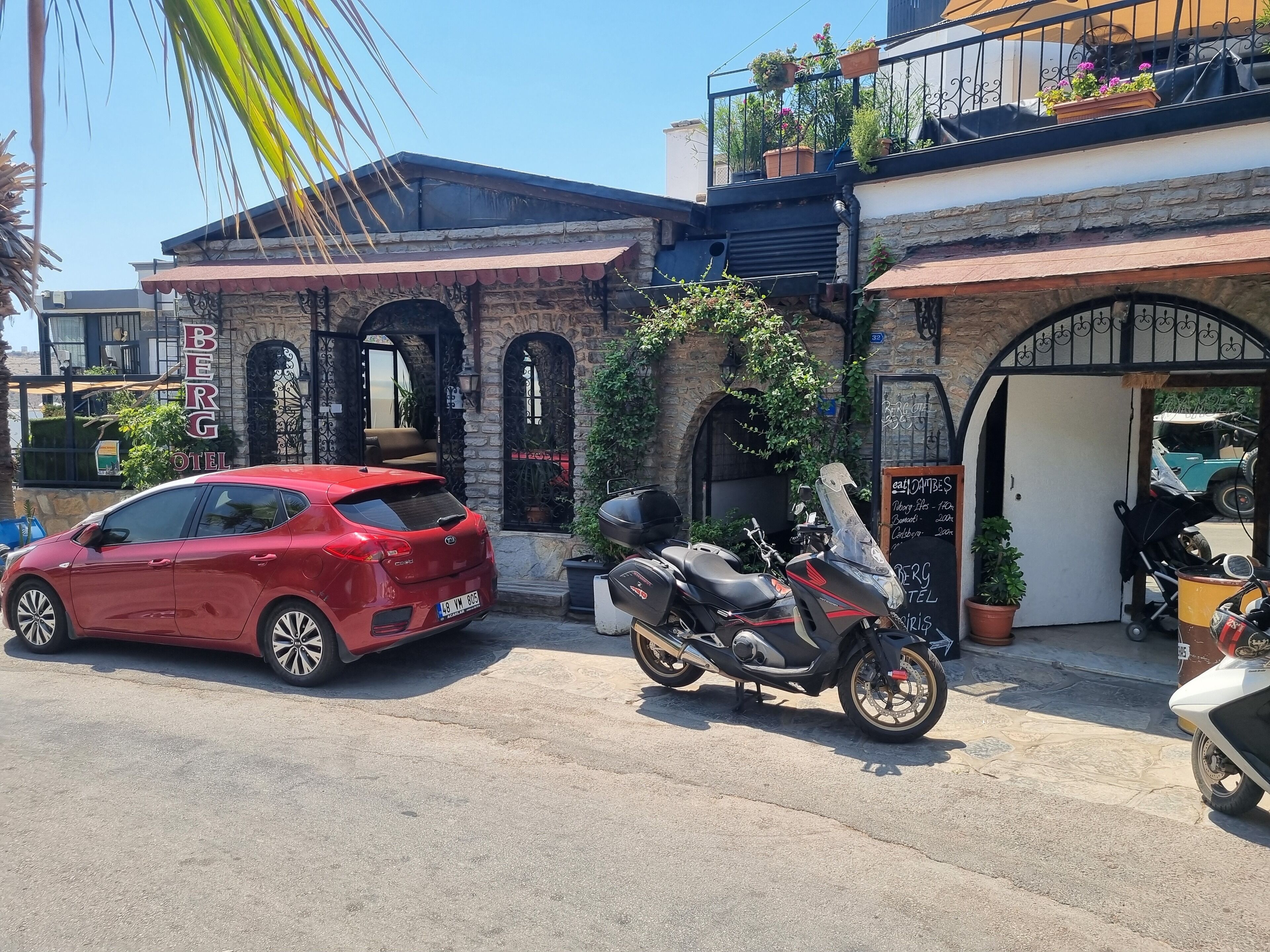 A red car parked in front of a building with a stone facade, a motorcycle, and a sign that reads "BERG HOTEL".