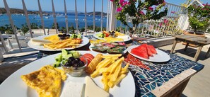 A table set with various breakfast items including eggs, cheese, and fruits, overlooking a scenic coastal view. - BERG OTEL (Bodrum)